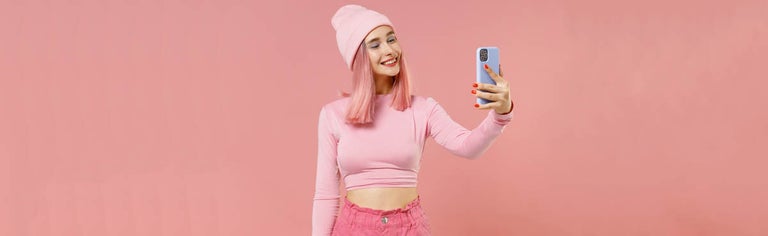 Young pink-haired woman using phone against pink background