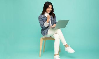 Smiling young dark haired woman using laptop against mint green background