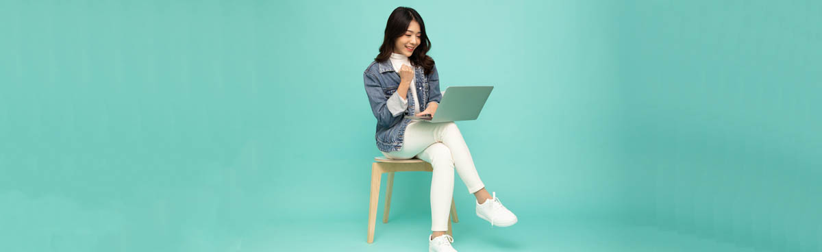 Smiling young dark haired woman using laptop against mint green background