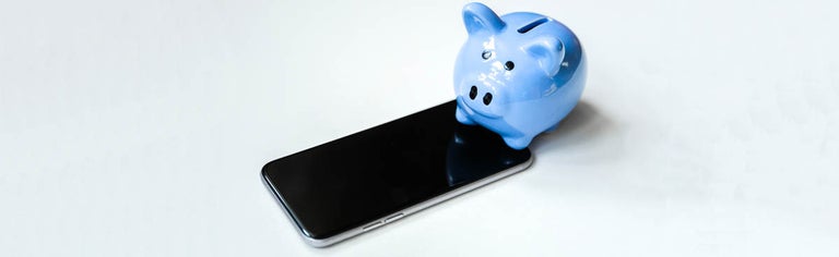 A blue piggy bank next to a mobile phone