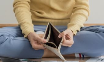 Person sitting on floor with bills, looking at empty wallet.