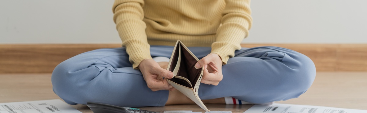 Person sitting on floor with bills, looking at empty wallet.