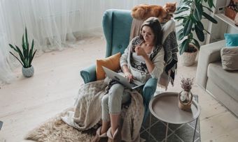 Woman using laptop by a fireplace with ginger cat on her chair