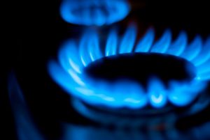 Natural gas stove top turned on with blue flame.