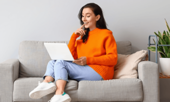 Young woman in orange jumper on white couch using laptop