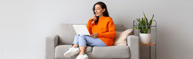 Young woman in orange jumper on white couch using laptop