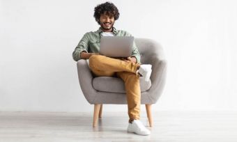 Young man in grey hoodie, sitting in chair and using a laptop