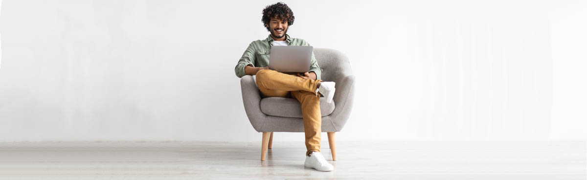 Young man in grey hoodie, sitting in chair and using a laptop