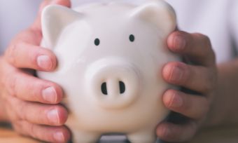 Hands holding white piggy bank in centre of table.