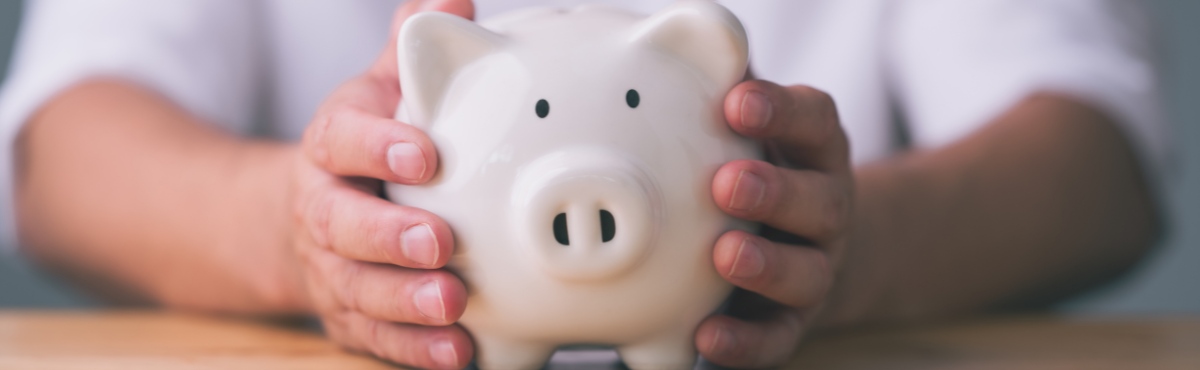 Hands holding white piggy bank in centre of table.