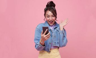 Happy young woman using phone with pink background