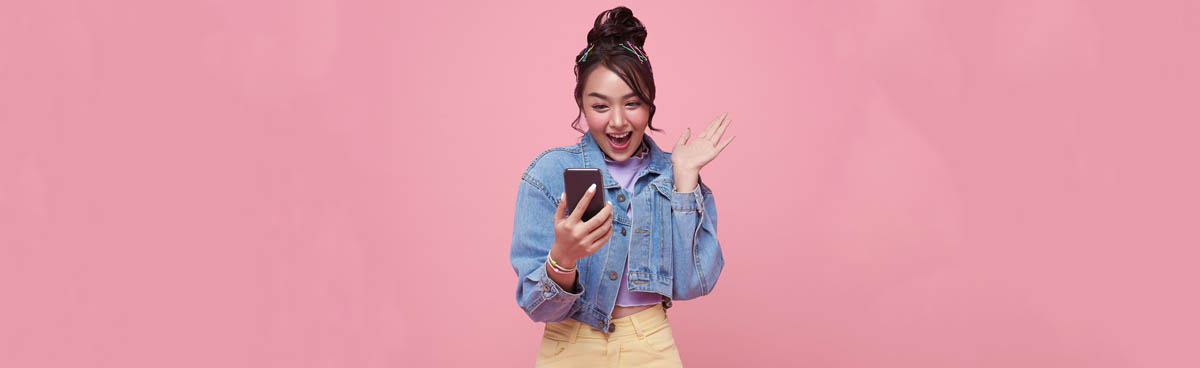 Happy young woman using phone with pink background