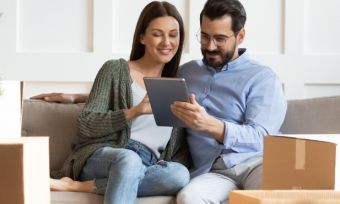 Happy couple looking at iPad in new house with boxes around them.