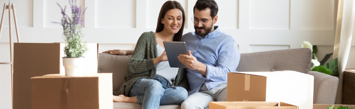 Happy couple looking at iPad in new house with boxes around them.