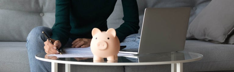Woman using laptop to pay bills with piggy bank