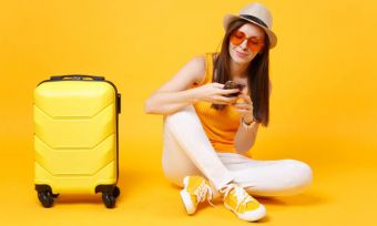 Woman with suitcase and orange outfit using phone