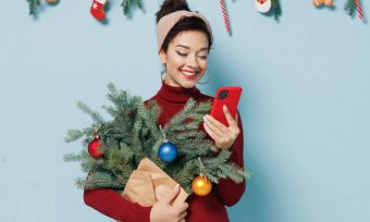 Smiling woman holding mini Christmas tree and looking at phone