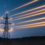 Powerlines with glowing yellow light along dark blue sky.