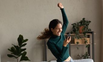 Woman happily dancing, looking at phone.