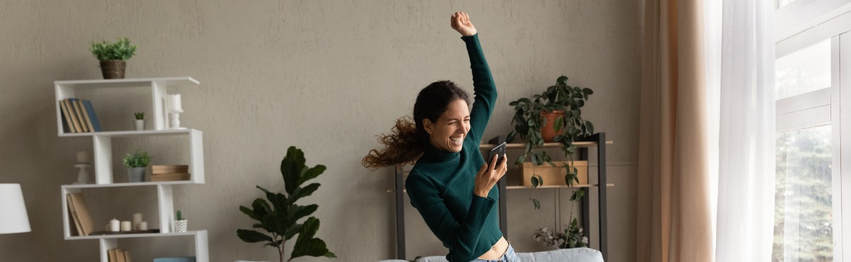 Woman happily dancing, looking at phone.