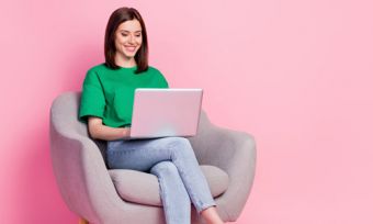 Woam sitting down looking at laptop against pink background