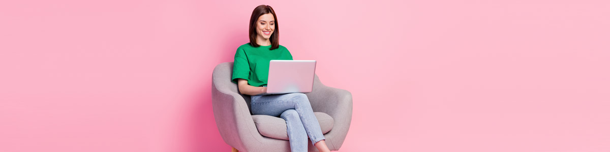 Woam sitting down looking at laptop against pink background