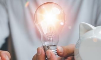 Man at desk holding lightbulb with piggy bank.