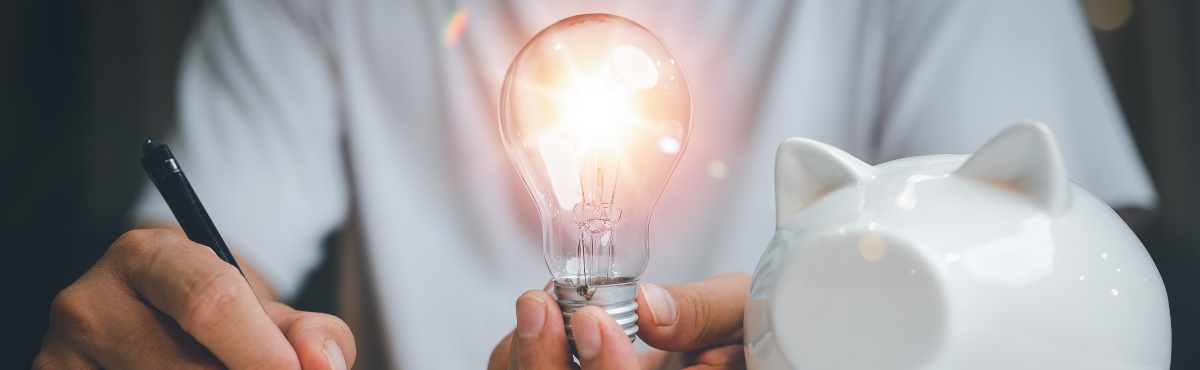 Man at desk holding lightbulb with piggy bank.