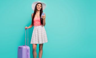 Woman looking at phone with suitcase against teal background