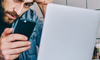 Man looking at phone with laptop nearby