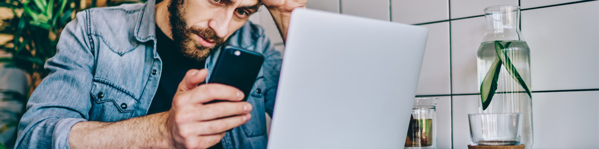 Man looking at phone with laptop nearby