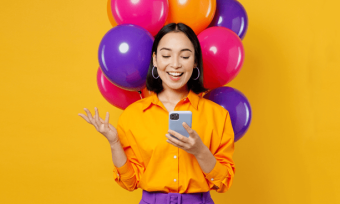 Celebrating woman with multicoloured balloons holding a mobile phone