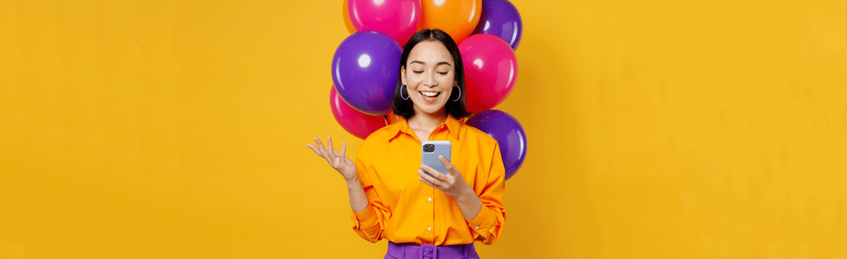 Celebrating woman with multicoloured balloons holding a mobile phone