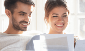 Happy couple sitting on couch, looking at bills.