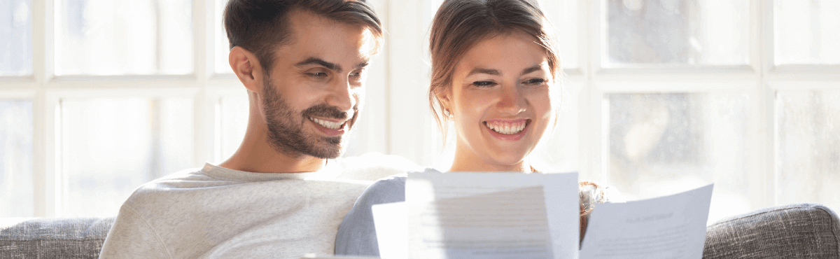 Happy couple sitting on couch, looking at bills.