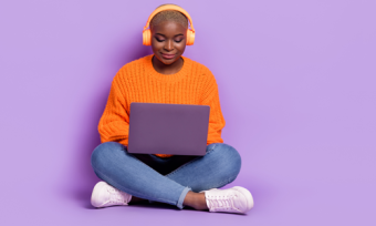 Woman wearing headphones and looking at laptop against purple background