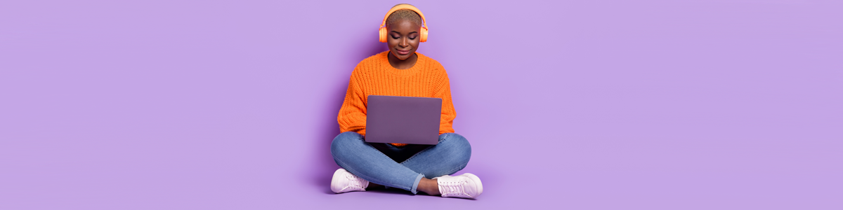 Woman wearing headphones and looking at laptop against purple background