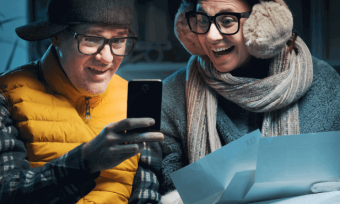 Couple in winter coats looking at bills, excited.