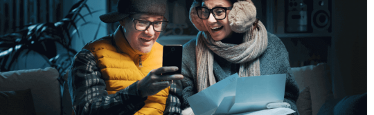 Couple in winter coats looking at bills, excited.