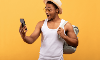 Smiling man with backpack using smartphone against orange background