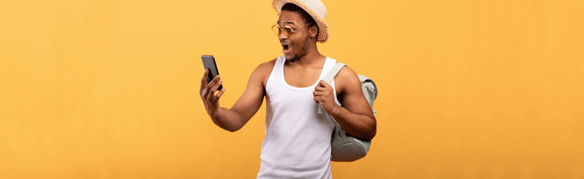 Smiling man with backpack using smartphone against orange background