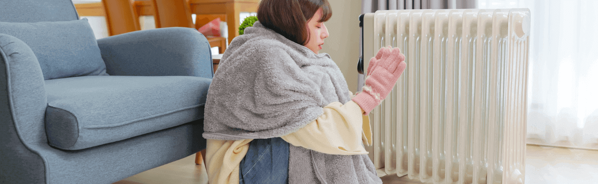 Woman in front of heater, wrapped in blanket, wearing gloves.