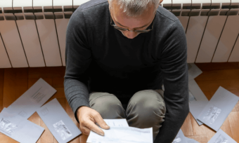 Old man looking at energy bills, worried, in front of heater.