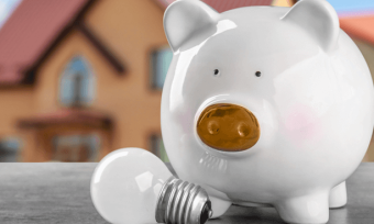 White piggy bank in front of toy house with light bulb