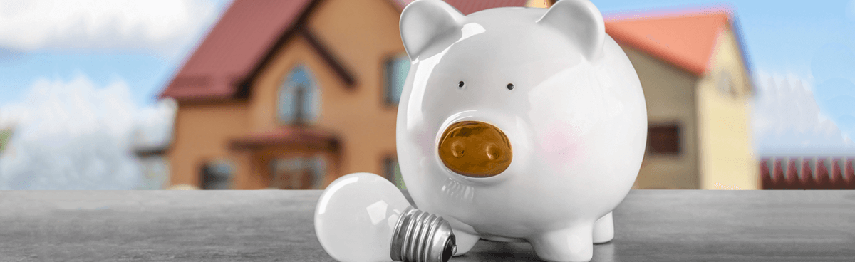 White piggy bank in front of toy house with light bulb