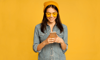 Happy woman using smartphone with yellow background