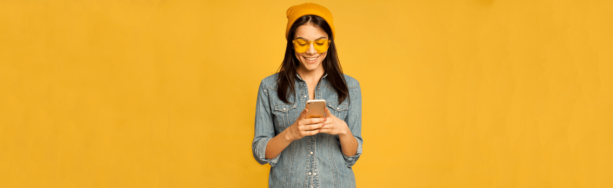 Happy woman using smartphone with yellow background