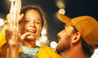 Father and child high-fiving in excitement, surrounded by outdoor lightbulbs.