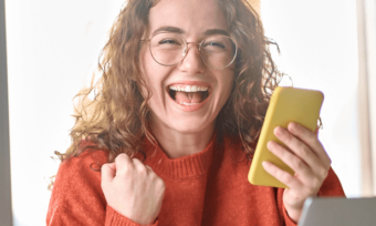 Girl in orange sweater excited by news on her phone.