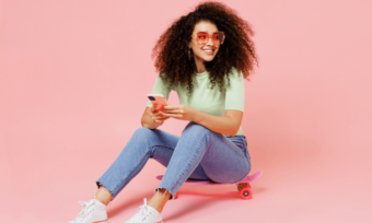 Happy woman sitting on skateboard, using phone